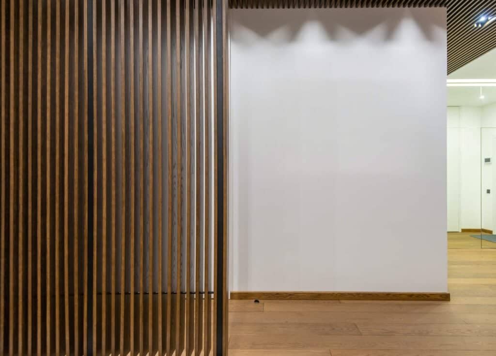 A slatted wooden screen separates two seating zones. Therefore, this modern setup illustrates split living room ideas that create boundaries without blocking light.