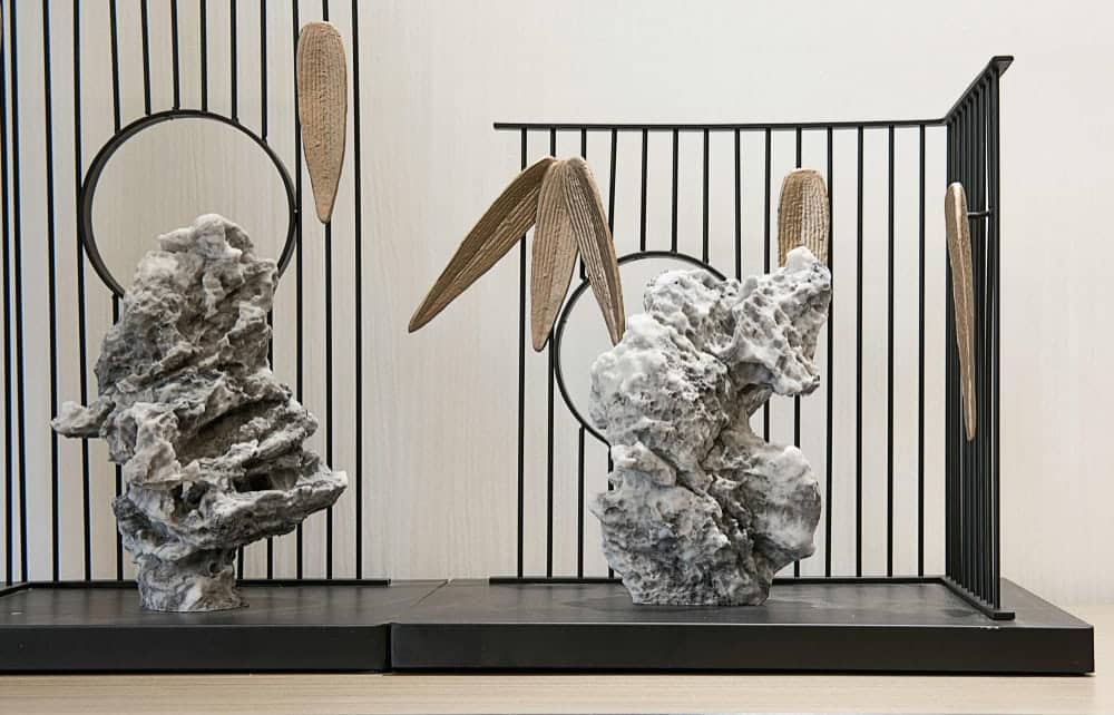 A tall sculpture placed between two seating areas. In this way, the art piece highlights split living room ideas that use design objects as soft dividers.