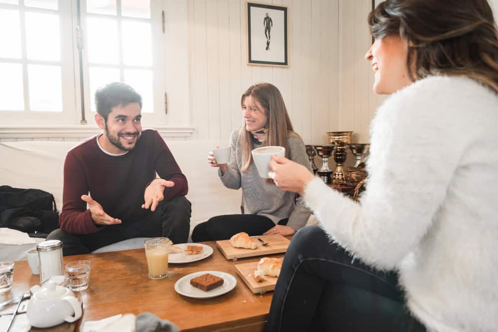 Three friends enjoying coffee and pastries around a wooden table, showing comfortable coffee table height for casual conversation.