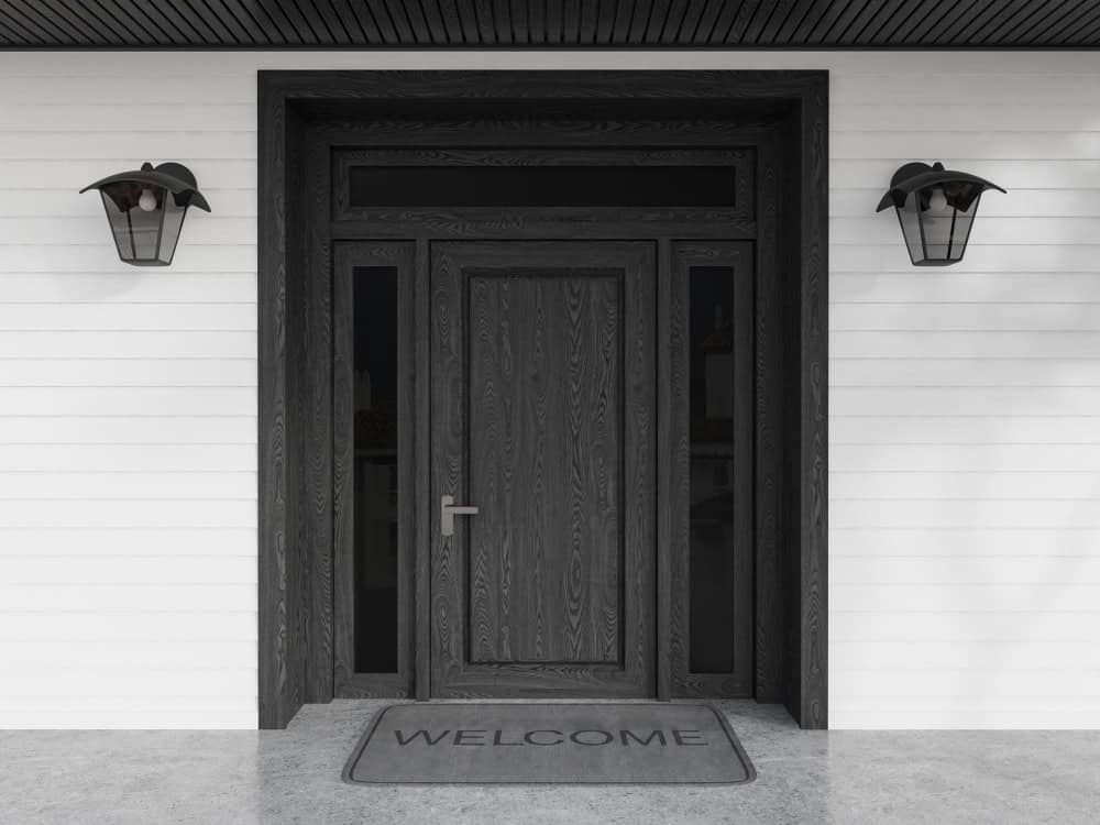 Front door of black and white wooden house with welcome mat entrance
