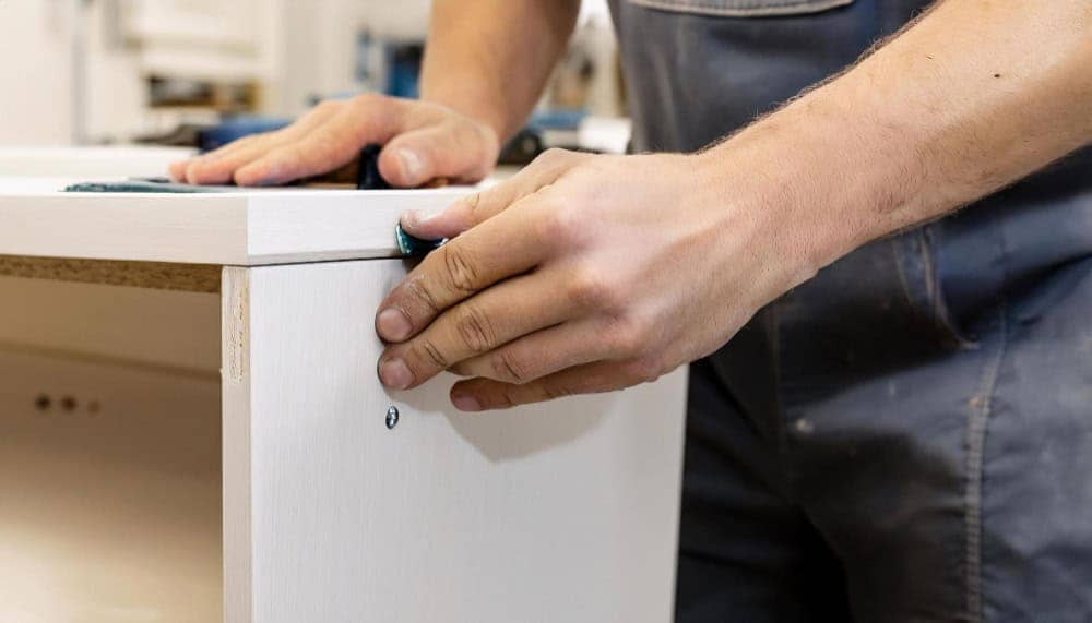 Close-up of hands assembling a DIY TV stand from light wood, showing precision craftsmanship and attention to detail in modern furniture building.