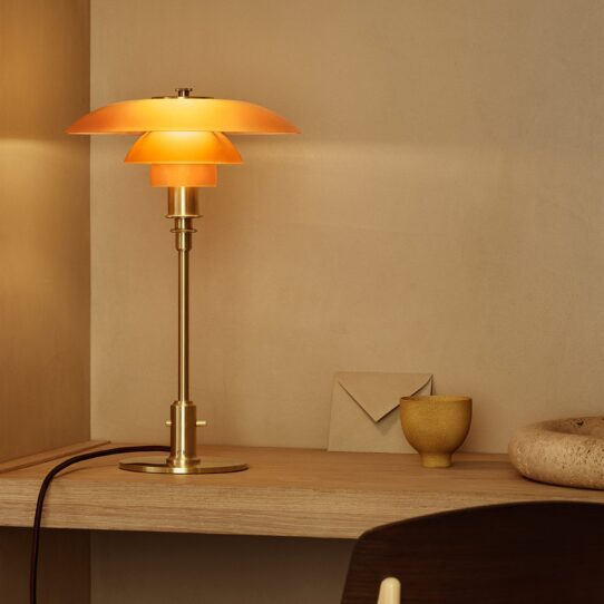 Pomelo Table Lamp can sits on a wooden table next to a stack of books and a potted plant.