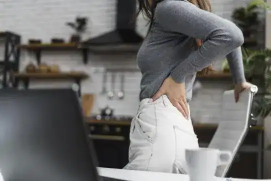 side view woman having backache while working from home - tips to prevent sciatica