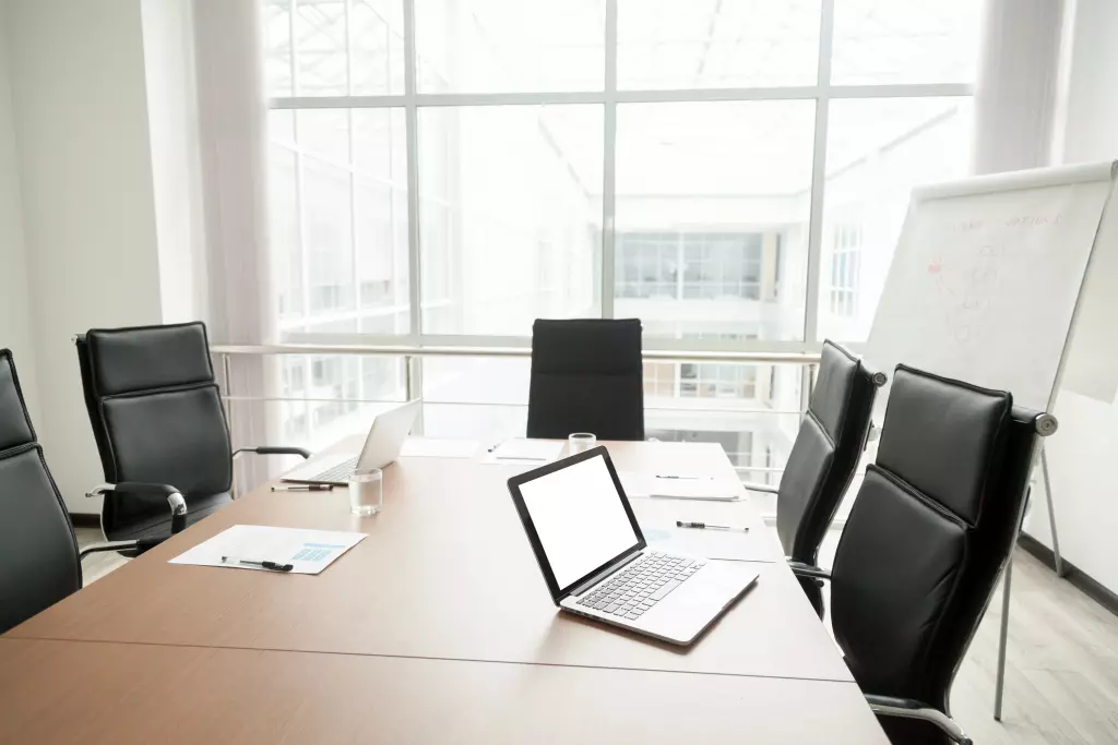 Minimalist Conference Room With A Large Rectangle Table, Black Ergonomic Office Chairs, And A Flip Boards.
