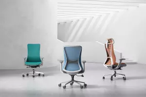 Three ergonomic office chairs in vibrant colors—teal, blue, and orange—displayed in a minimalist workspace with clean lines and a modern design.