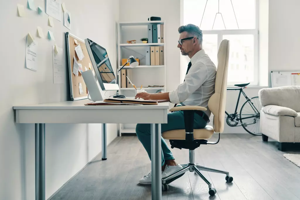 A tall man in a white shirt and tie working at his desk, sitting comfortably in an ergonomic office chair.