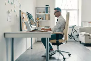 A tall man in a white shirt and tie working at his desk, sitting comfortably in an ergonomic office chair.