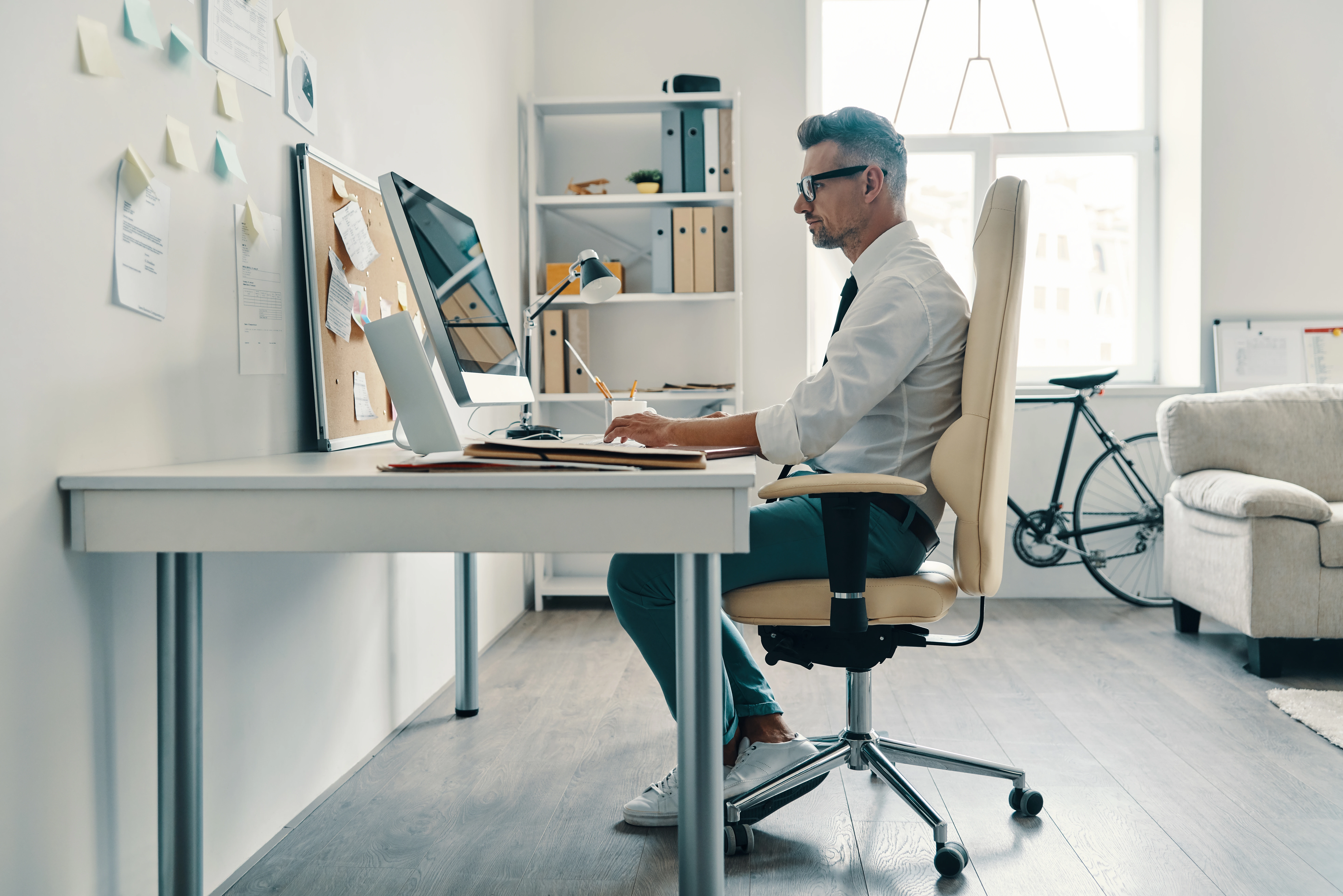 A tall man in a white shirt and tie working at his desk, sitting comfortably in an ergonomic office chair.