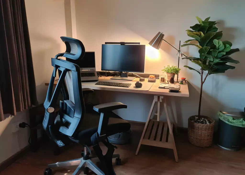 A modern home office setup featuring a black ergonomic office chair, a large monitor, a laptop, and a stylish desk lamp.