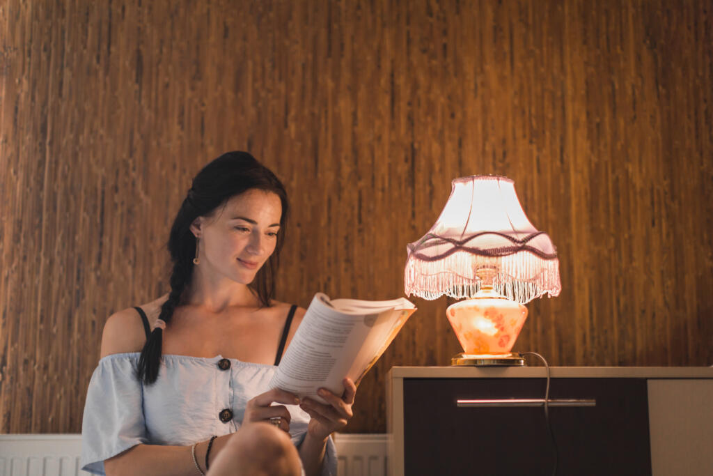 young woman reading book near illuminated light lamp