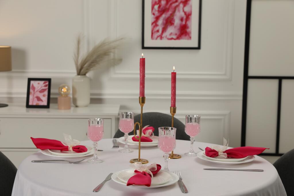 Color accent table setting. Glasses, plates, burning tapers and red napkins on dining table