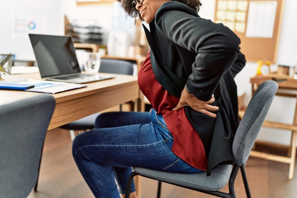 young african american woman suffering backache working office | Sohnne®  tips to prevent sciatica
