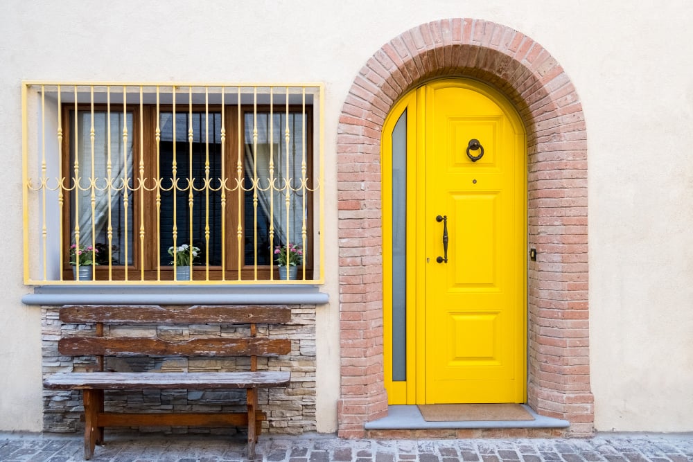 A view of the facade of the house with a wooden bench and a yellow door