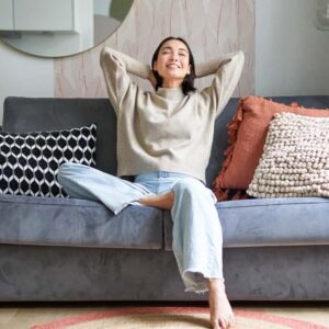 Woman relaxing on a cozy sofa with textured pillows showing decorating apartment ideas that blend comfort and style.