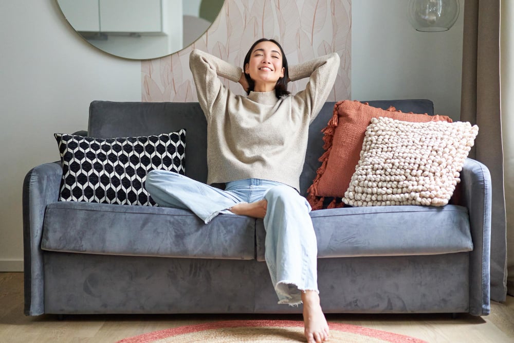 148342 | Sohnne® Woman relaxing on a cozy sofa with textured pillows showing decorating apartment ideas that blend comfort and style.