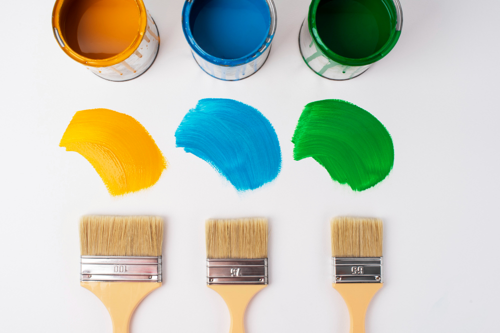 diy tv stand color | Sohnne® Three paint brushes and cans of yellow, blue, and green paint arranged on a white surface, showing how different colors can transform and personalize a DIY TV stand.