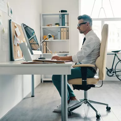 A tall man in a white shirt and tie working at his desk, sitting comfortably in an ergonomic office chair.